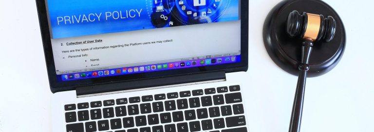 laptop Laptop einer Namensagentur mit offener Seite zu Datenschutzrichtlinien und einem Richterhammer daneben.