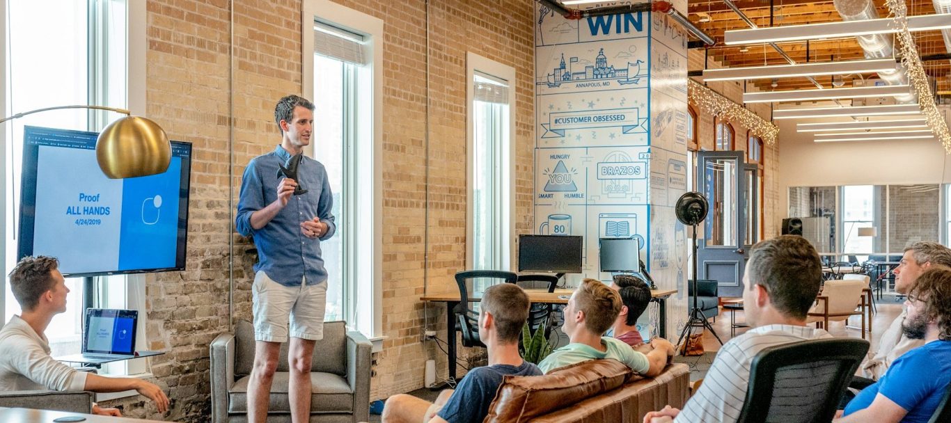 meeting Ein Mann präsentiert vor einer Gruppe von Personen in einem modernen Büro für Firmennamen finden.